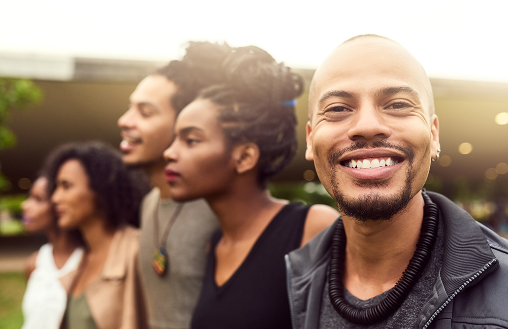 Group of friends looking off into distance with one happy, smiling man in the front looking at you